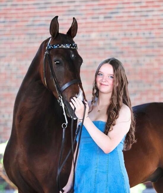 Fiona wearing a blue dress from TEC Connections Academy pictured here with her hand on her brown horse.